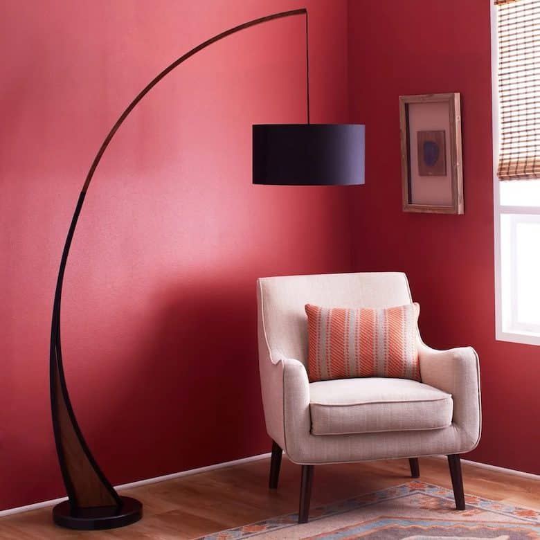 Cozy corner with a beige armchair, striped throw pillow, arched floor lamp, and red walls